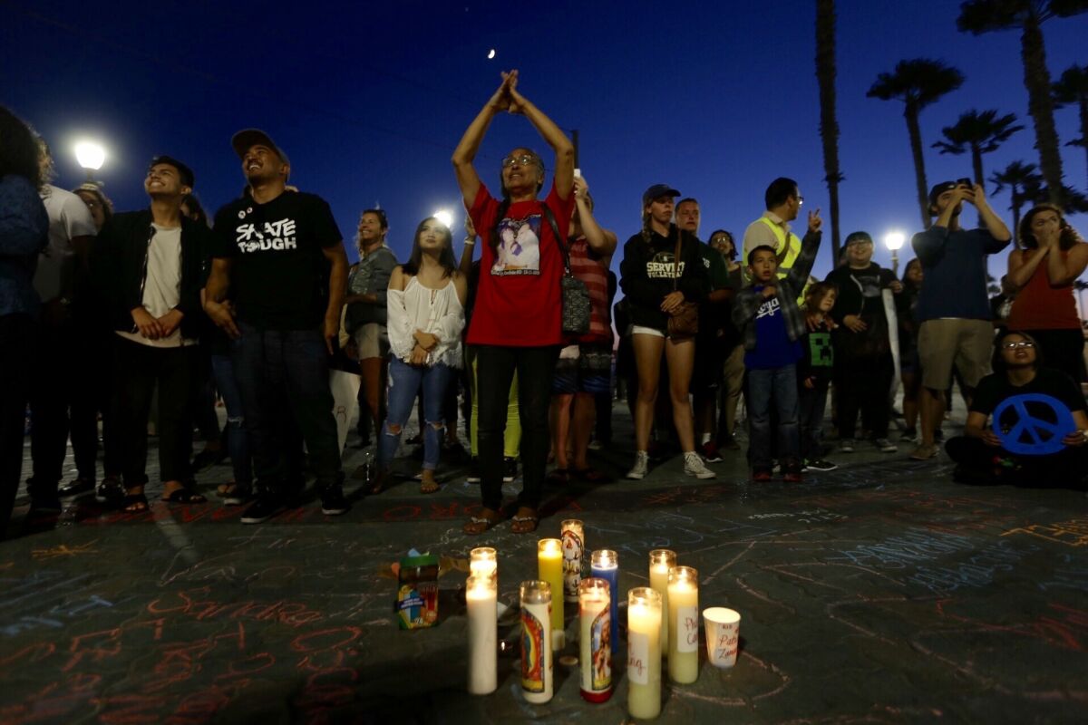 Theresa Smith, center, of Placentia, joins about two dozen people at a vigil at the Huntington Beach Pier for victims of violence.