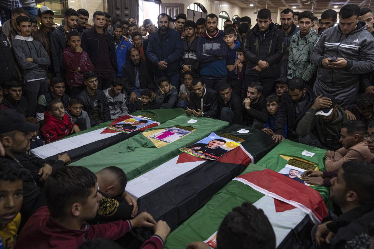 Men gather around four coffins, three of which are draped with Palestinian flags