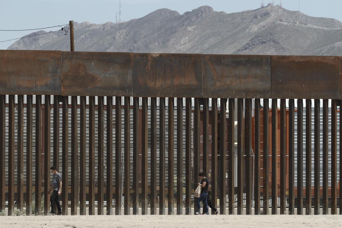 FILE - In this July 17, 2019, file photo, three migrants who had managed to evade the Mexican National Guard and cross the Rio Grande onto U.S. territory walk along a border wall set back from the geographical border, in El Paso, Texas, as seen from Ciudad Juarez, Mexico. The Department of Homeland Security is moving $271 million from other agencies such as FEMA and the U.S. Coast Guard to fund immigration detention beds and support its policy forcing asylum seekers to wait in Mexico. (AP Photo/Christian Chavez, File)