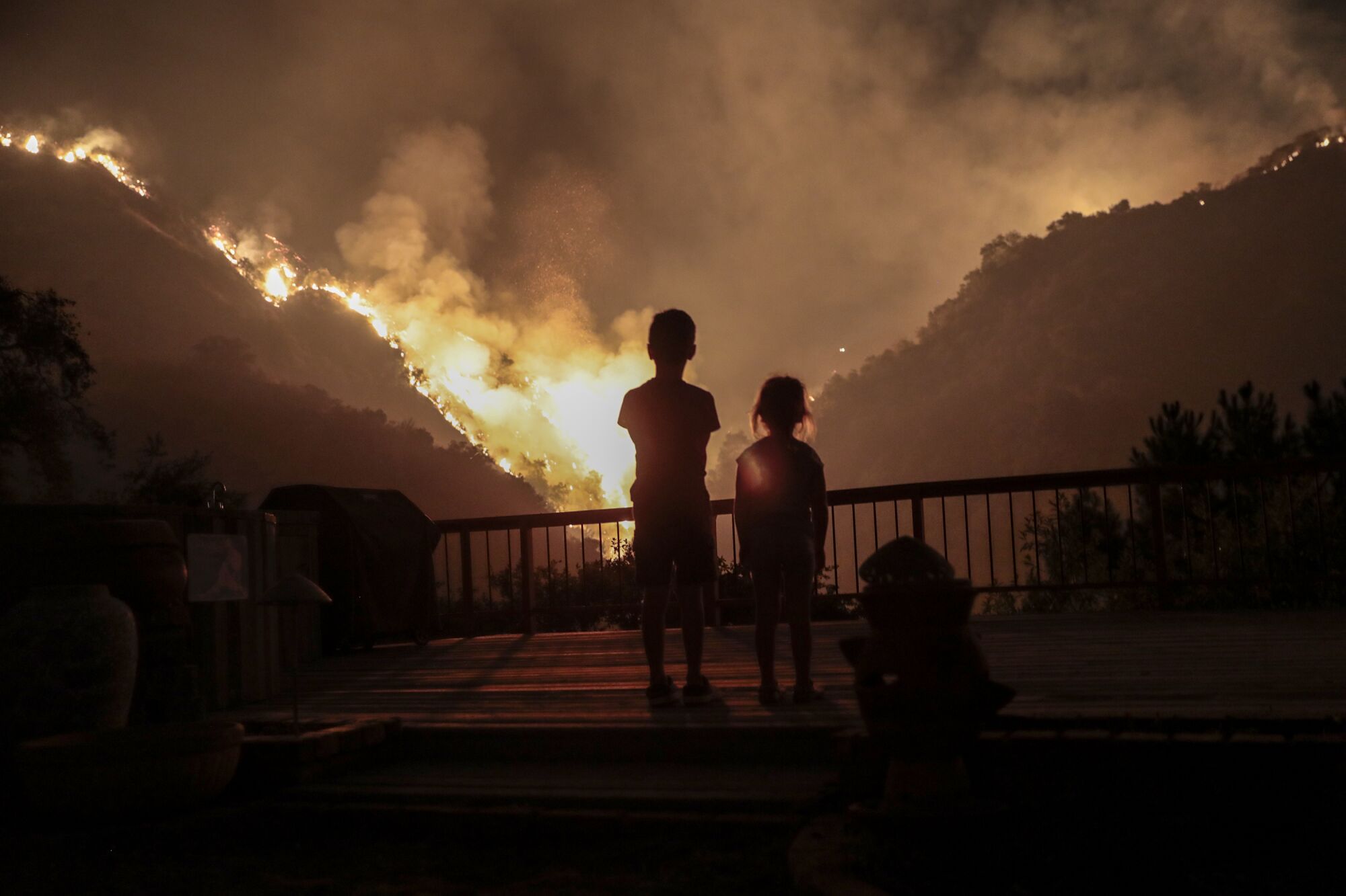 Iris, 4, and Castle Snider, 8, look on as flames from a controlled burn engulf the hillsides behind their backyard.