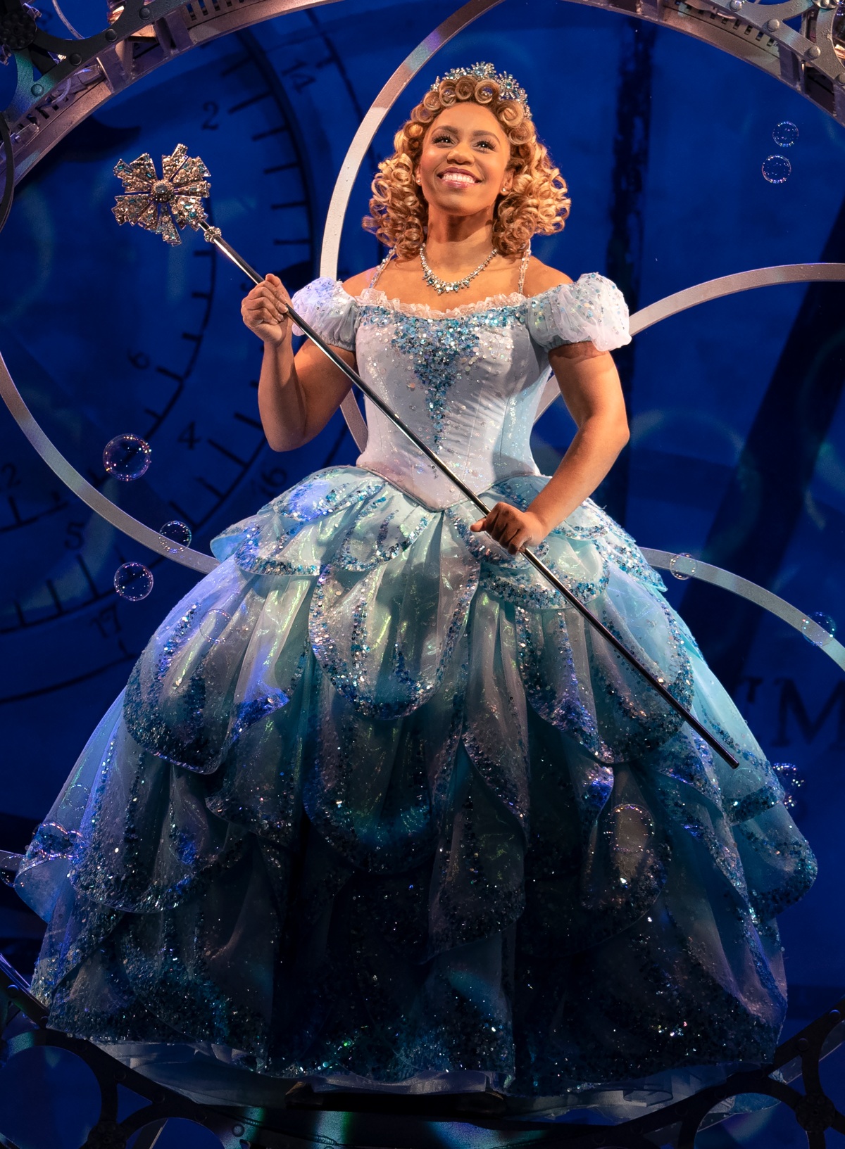 A woman with curly blond hair wearing a blue ballgown and wielding a magic scepter