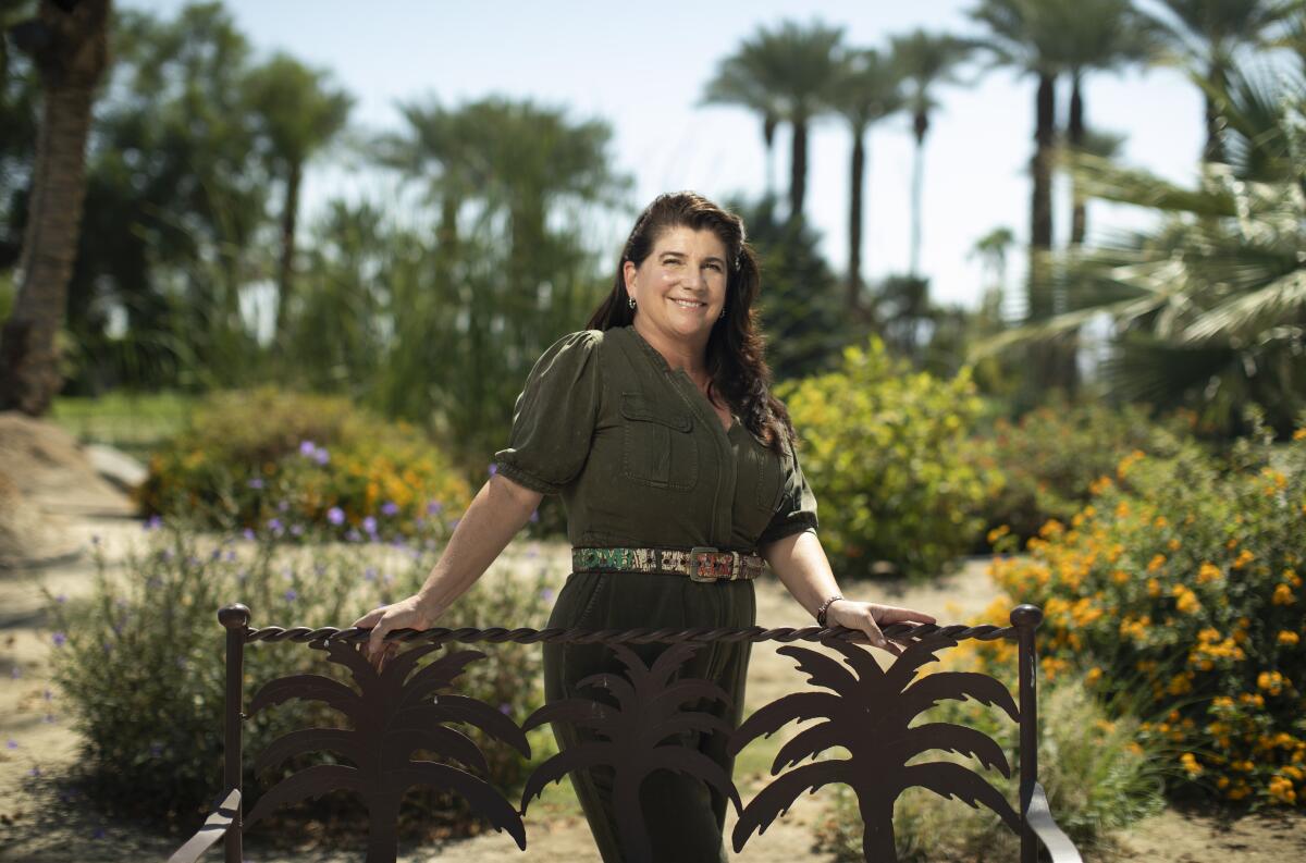 A woman stands against an ornamental fence with palm tree silhouettes.