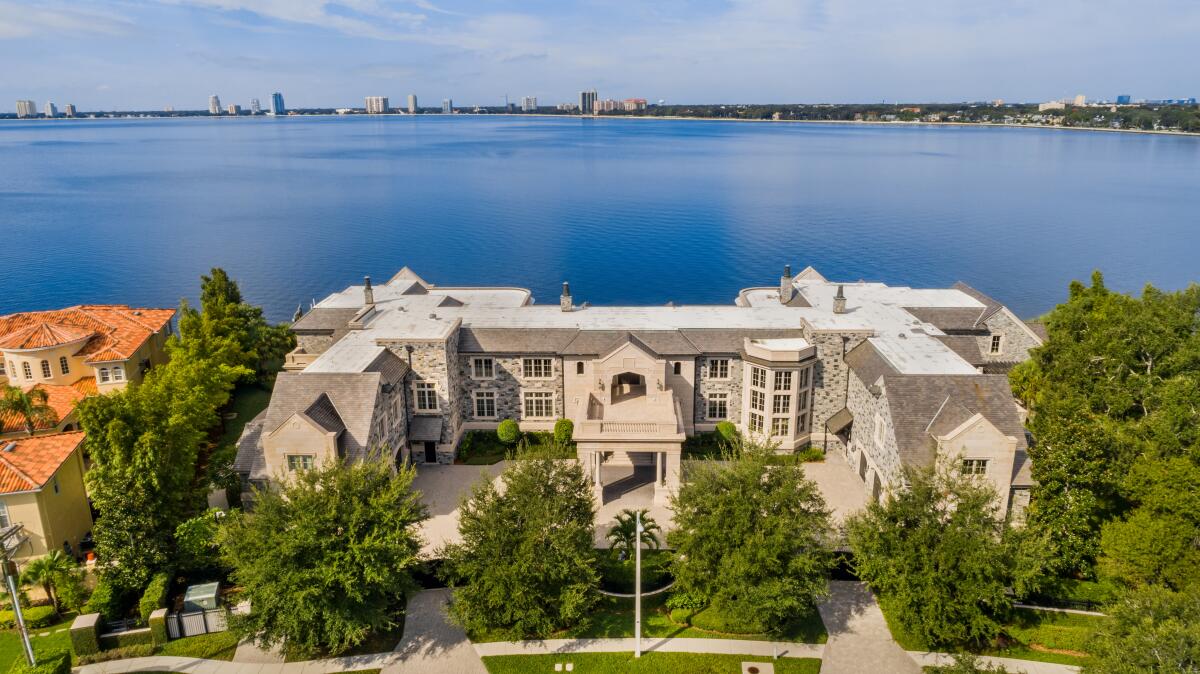 Aerial view of a mansion with an expanse of water in the back and trees in front.