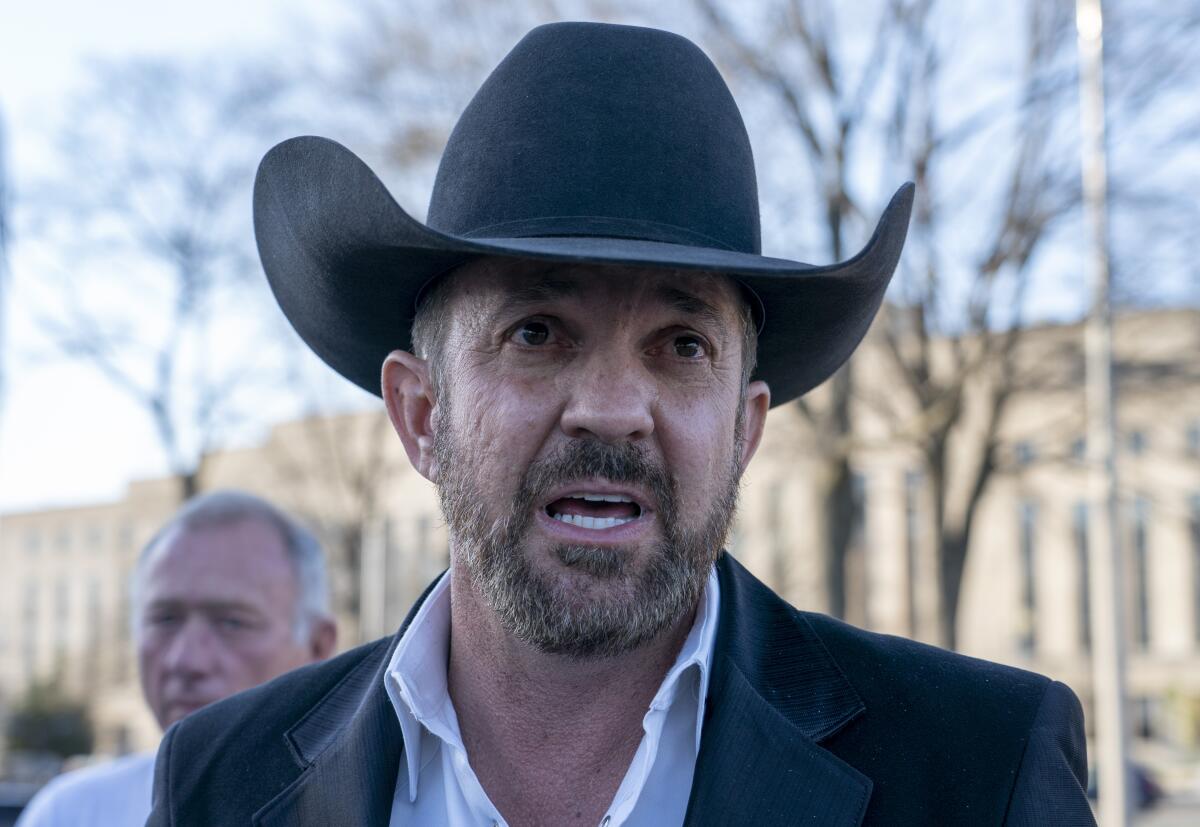 A man in a cowboy hat speaks to reporters 
