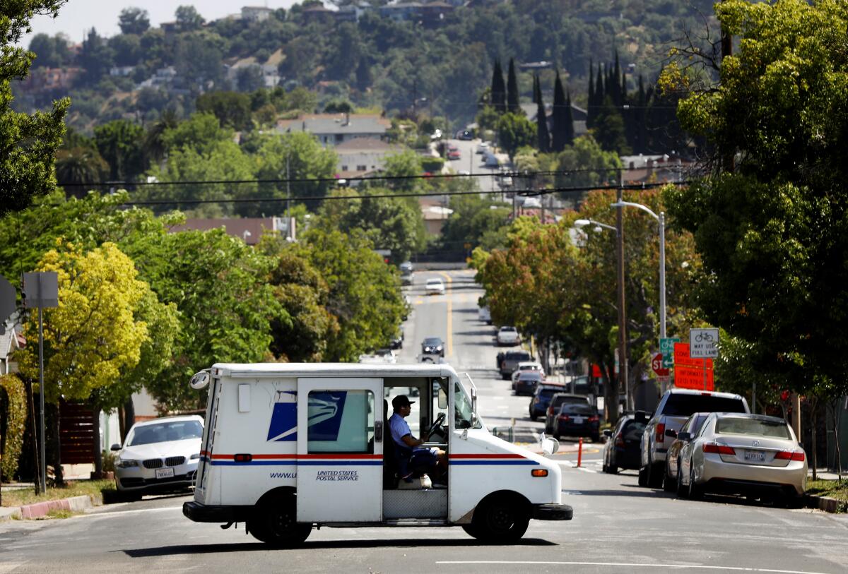 A mail truck passes crosses intersection at bottom of a hill