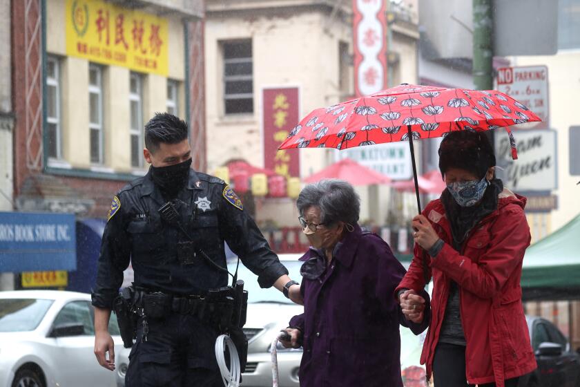 SAN FRANCISCO, CALIFORNIA - MARCH 18: San Francisco police officer William Ma (L) helps an elderly woman cross the street while on a foot patrol in Chinatown on March 18, 2021 in San Francisco, California. The San Francisco police have stepped up patrols in Asian neighborhoods in the wake of a series of shootings at spas in the Atlanta area that left eight people dead, including six Asian women. The San Francisco Bay Area is also seeing an increase in violence against the Asian community. (Photo by Justin Sullivan/Getty Images)