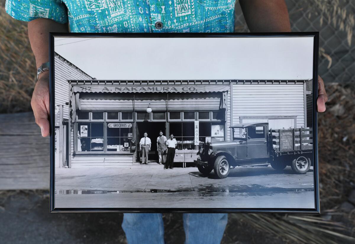 A person holding a large frame with a black-and-white photo of a vintage truck and three people outside a small store.