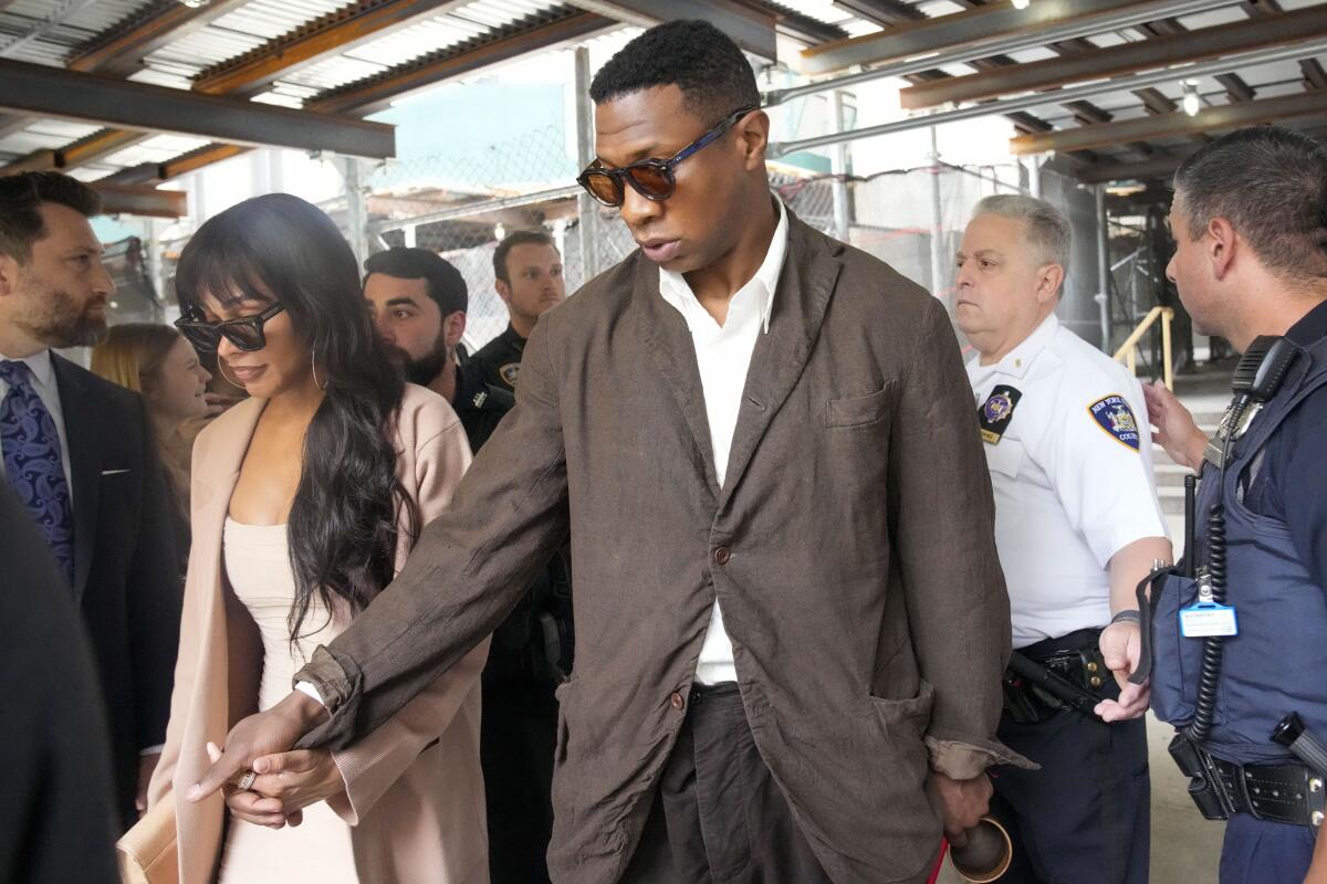 Jonathan Majors, center, and Meagan Good leave court while holding hands.
