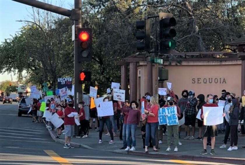 Parents holding signs demonstrate on a street corner.
