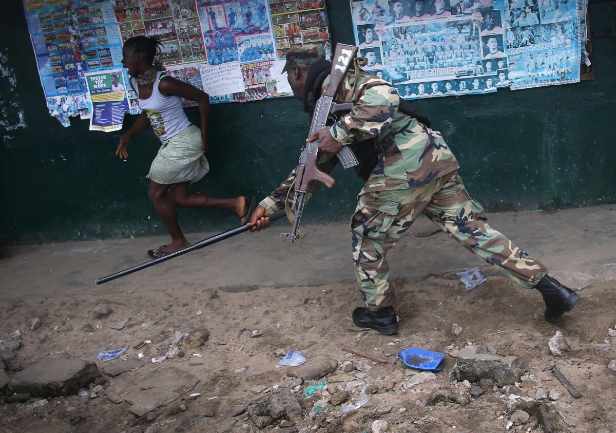 A Liberian soldier chases away a resident while enforcing a quarantine on the West Point slum in Monrovia.