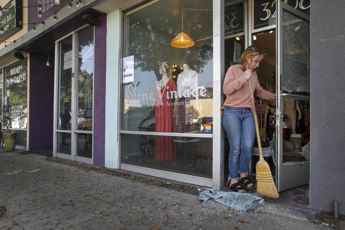 A woman sweeps broken glass in front of a store entrance