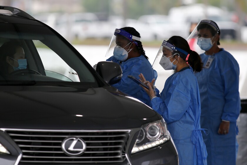 Workers collect a driver's information during a COVID-19 self-administering testing site at the O.C. fairgrounds.