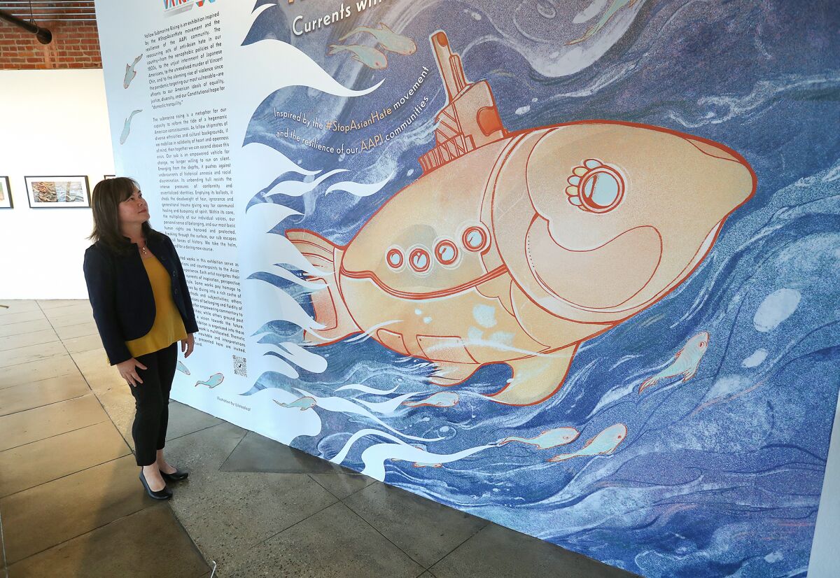 Curator Thuy Tran stands at the "Yellow Submarine Rising: Currents Within Asian American Art" marquee piece.