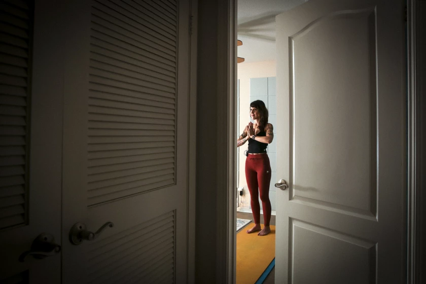 Laura Schwartz, vista através de uma porta aberta, pratica ioga em um tapete amarelo. 