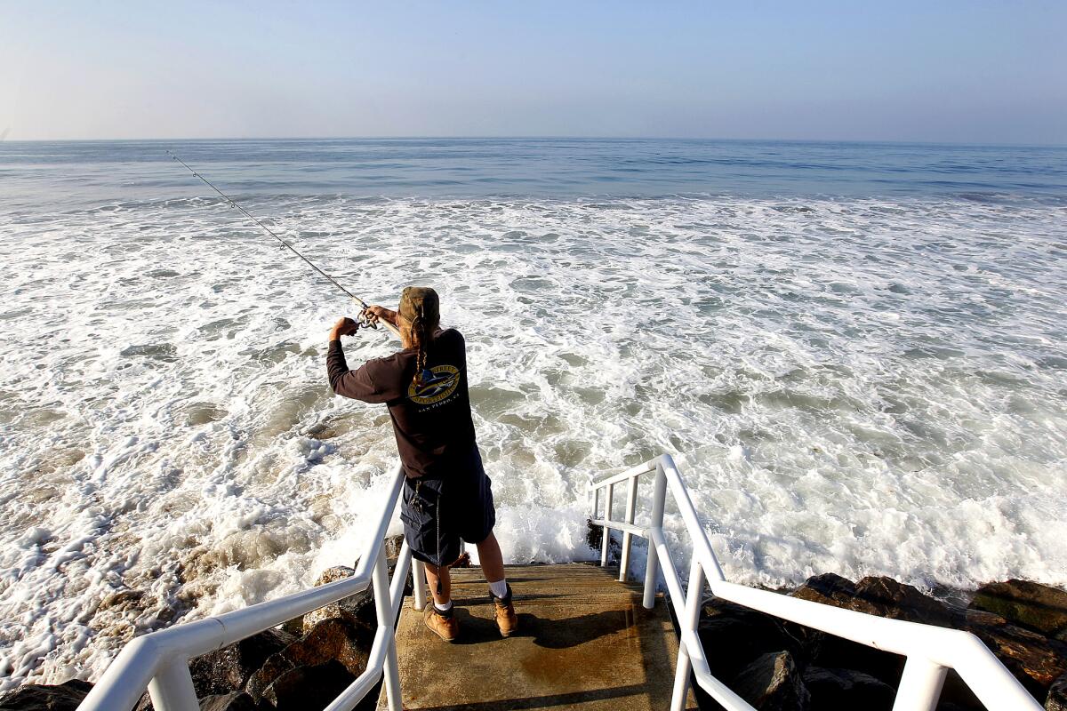 A man fishes during high tide in Malibu