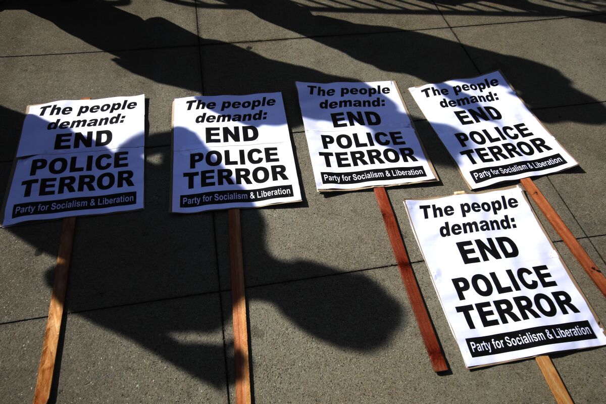 Protest signs that read "End Police Terror" on a sidewalk with people's shadows
