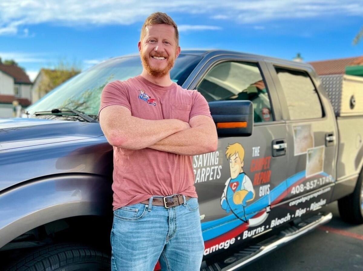 A smiling man with arms crossed stands next to a truck.