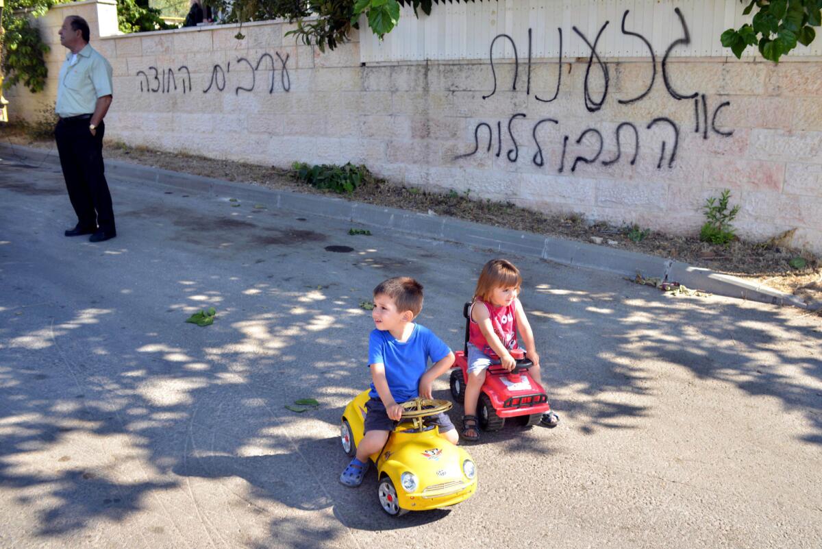An Israeli Arab man and children are seen on a street next to Hebrew graffiti that reads, "Racism or assimilation" and "Arabs out" on June 18 in the village of Abu Ghosh near Jerusalem. In an unrelated act that some attribute to racist attitudes, Israeli teenagers were sentenced Monday in the beating of an Israeli Arab youth in August 2012.