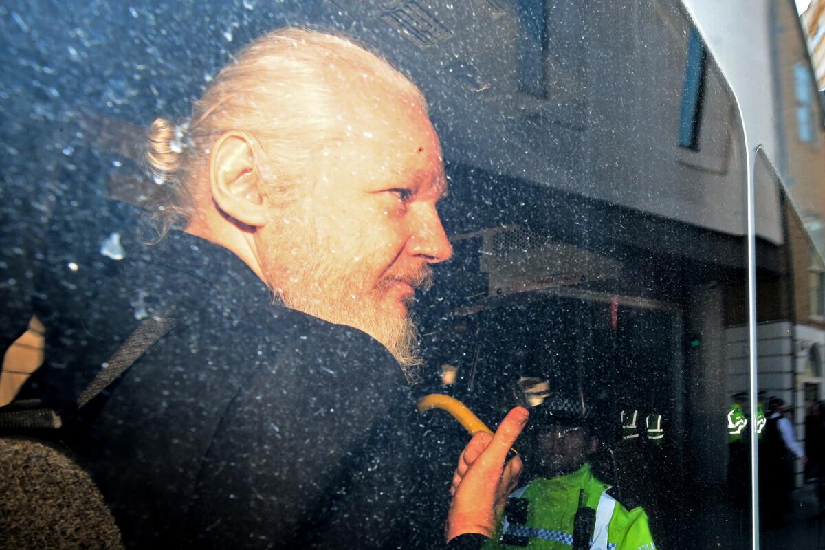 Julian Assange gestures to the media from a police vehicle on his arrival at Westminster Magistrates court Thursday in London.