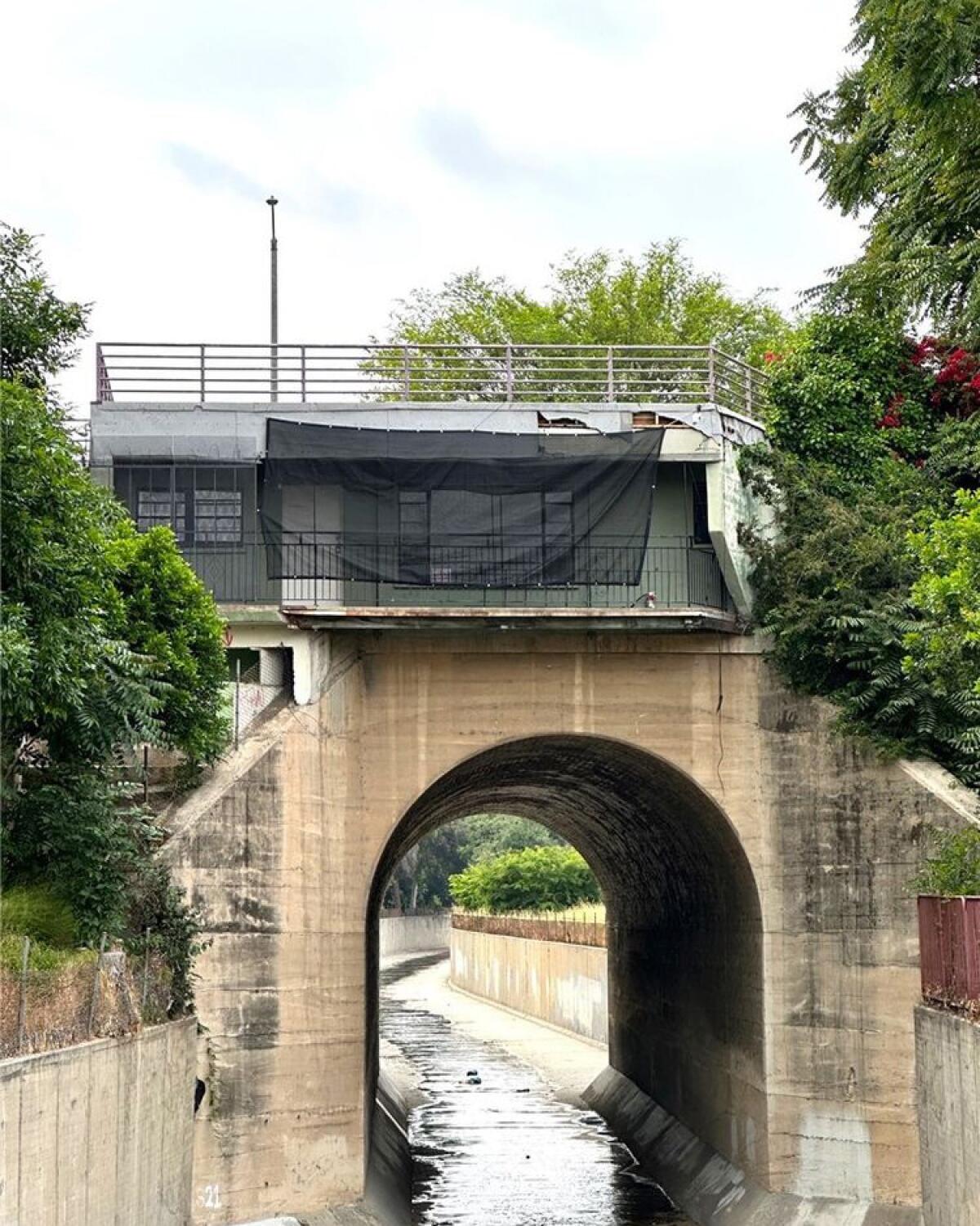 A vertical frame of a one-story dwelling sitting atop a water-canal bridge.