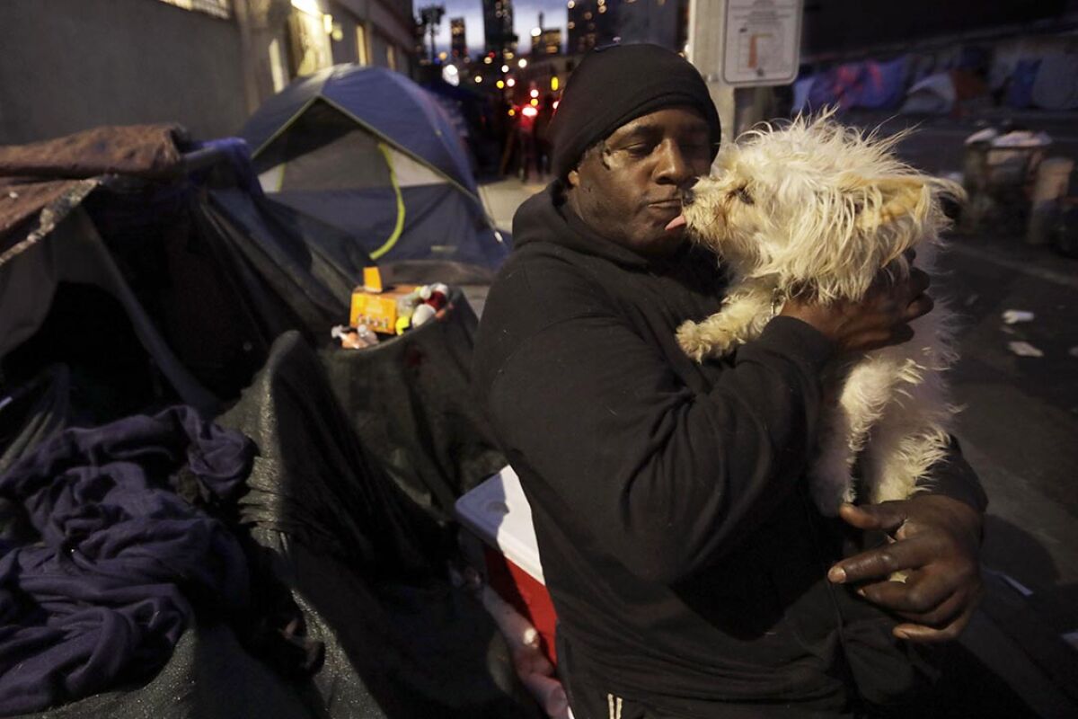 A man hugs his small yellow dog outside a tent on skid row.