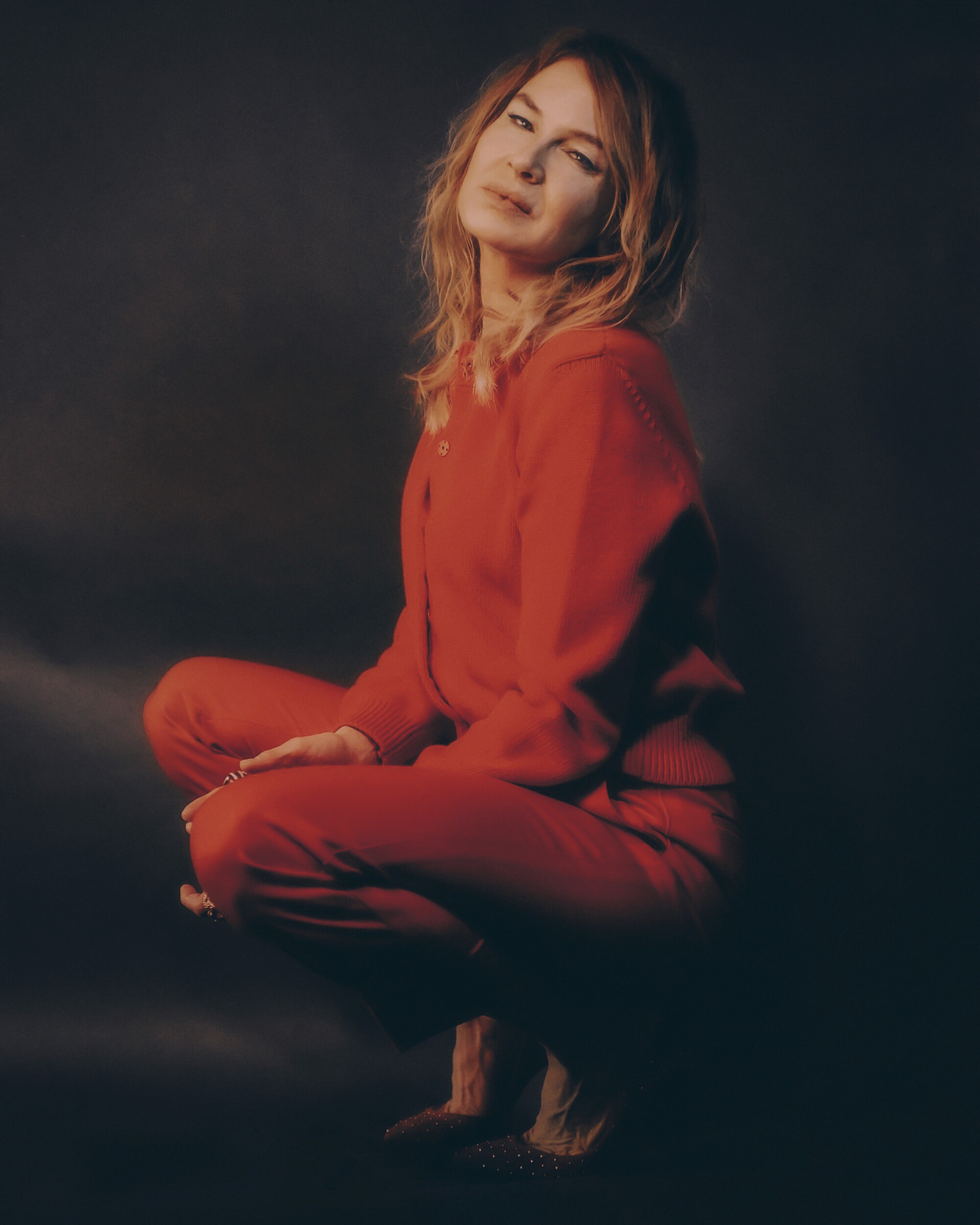 A woman in a red outfit poses in a crouch for a portrait