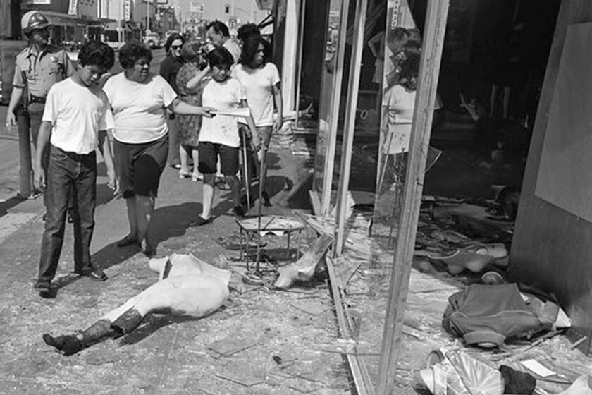 Passerby view smashed store windows and broken mannequin following the August 29, 1970 riot during the Chicano Moratorium march.