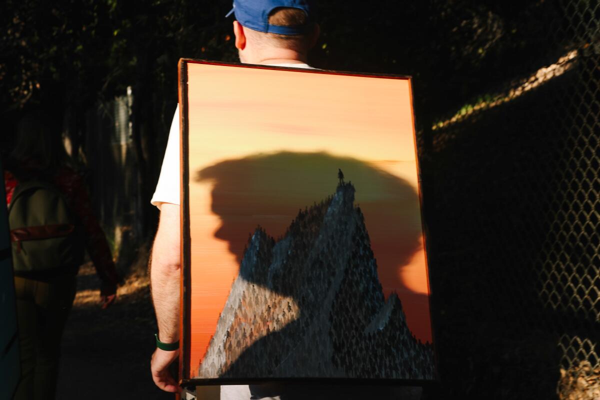 Art lovers, wearing paintings on their backs, participate in a sunset art hike to the top of a Griffith Park trail.