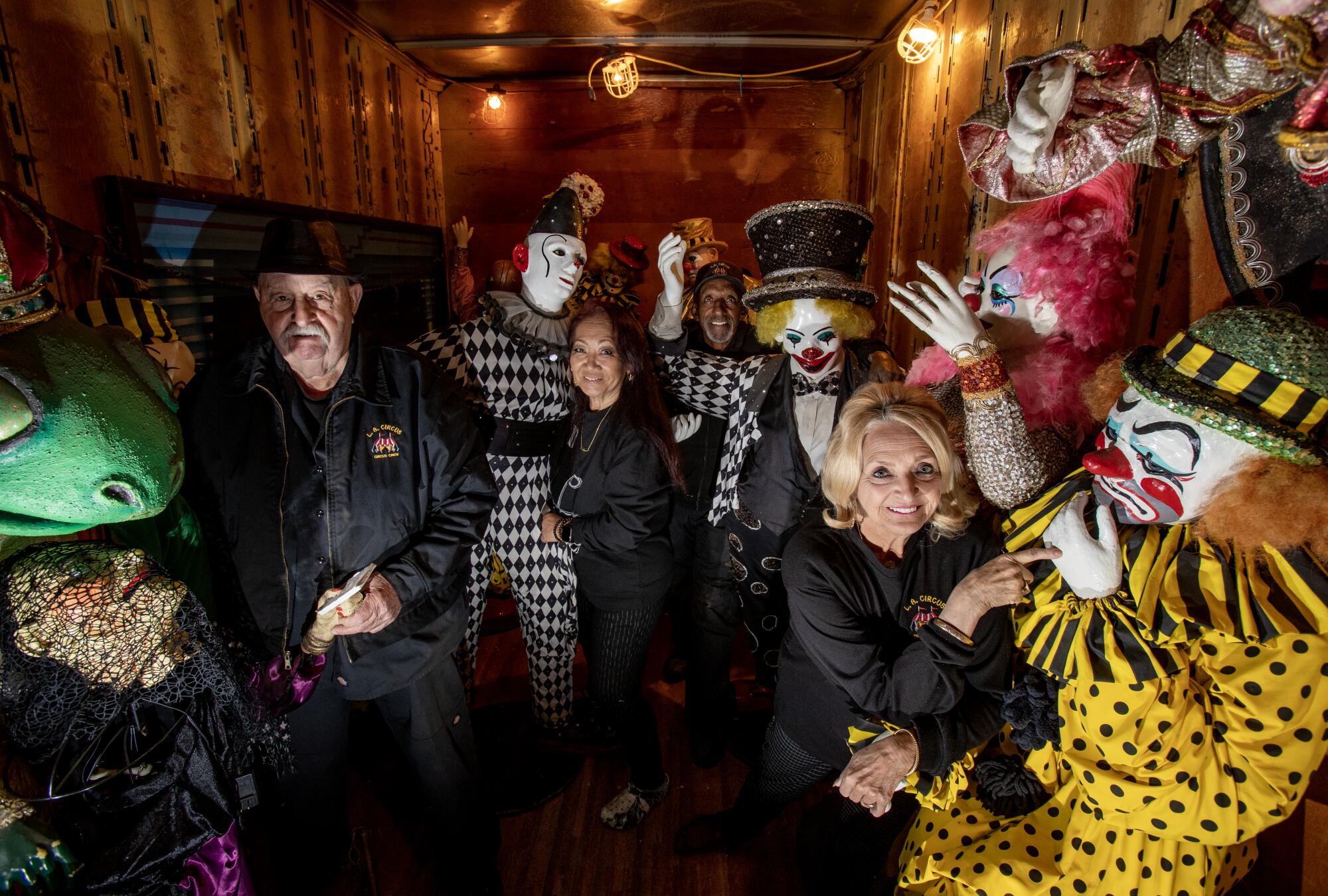 People stand next to clown statues in a prop house.
