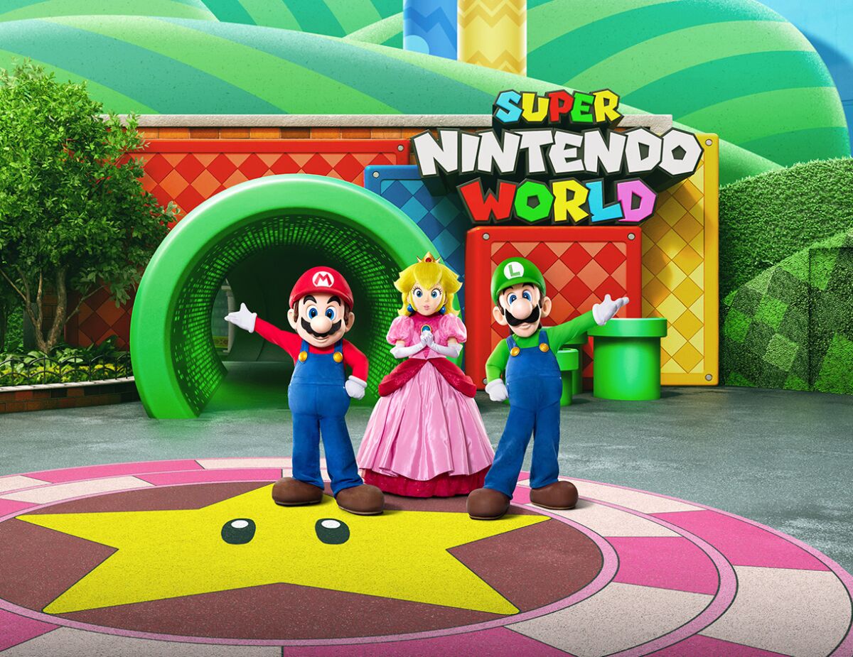 Colorful Super Mario characters gesture to a sign that says Super Nintendo World.