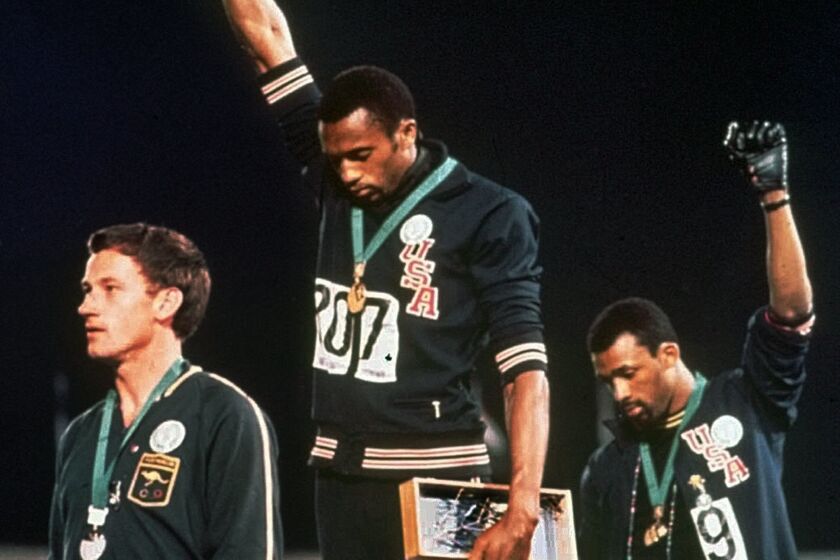 U.S. athletes Tommie Smith, center, and John Carlos stare downward while extending gloved hands skyward in 1968 