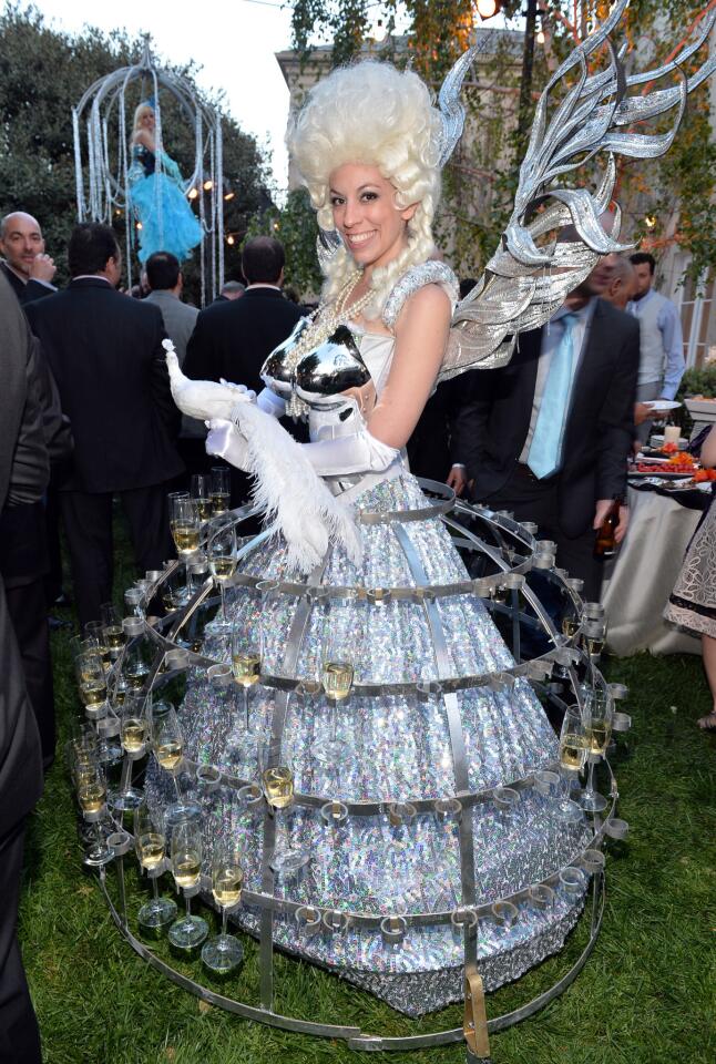 Another performer in period costume (adorned with wings) serves champagne from a hoop skirt constructed of metal.