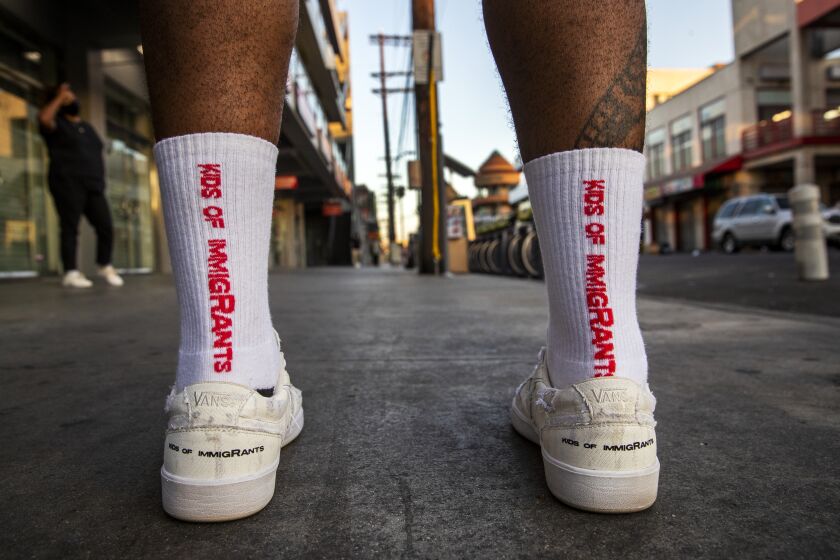 LOS ANGELES, CA - SEPTEMBER 29: Weleh Dennis, co-founder, of Los Angeles-based streetwear upstart Kids of Immigrants, wears their socks and their new collaboration shoes with Vans, called Work a Day in Our Shoes, Tuesday, Sept. 29, 2020 in the Los Angeles fashion district. Buezo, whose parents immigrated to the U.S. from Honduras, and Dennis, started their brand a few years ago and celebrities like Bad Bunny, Odell Beckham Jr. and Kehlani have been seen wearing their designs. This profile will focus on their origin stories as well as their upcoming shoe collaboration with Vans, which releases on Oct. 2. They are calling the shoe Work a Day in Our Shoes to celebrate the owner's immigrant roots, their parents and the overall working class community. (Allen J. Schaben / Los Angeles Times)