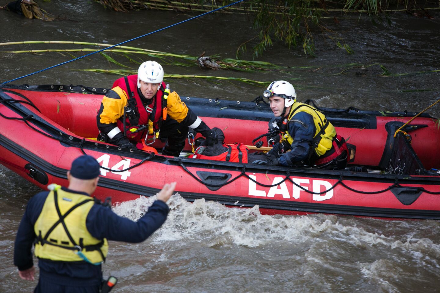 Fire Department swift water rescue members make their way across the storm-swollen Los Angeles River after rescuing a woman.