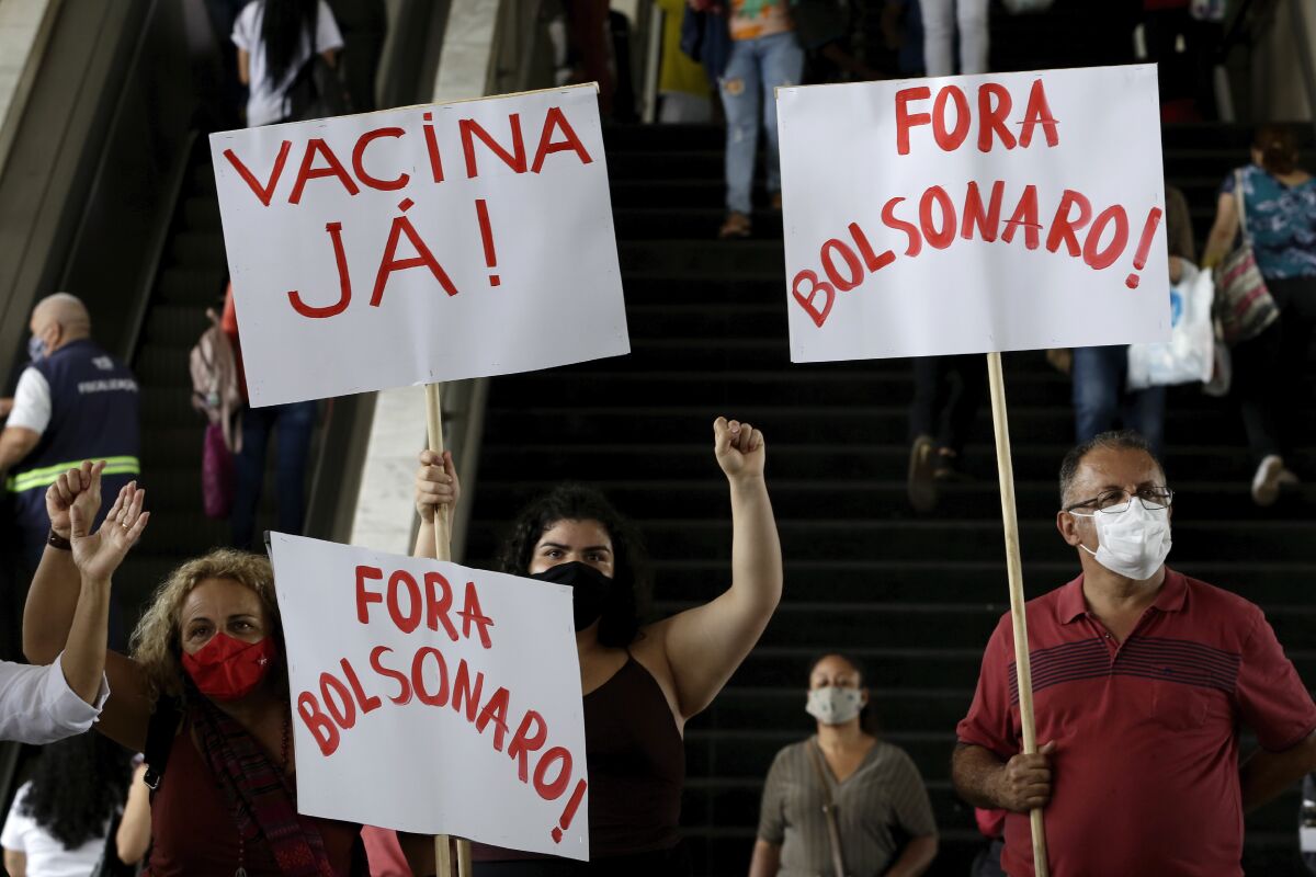 People at a bus station in Brasilia, Brazil, hold up signs protesting at President Jair Bolsonaro.