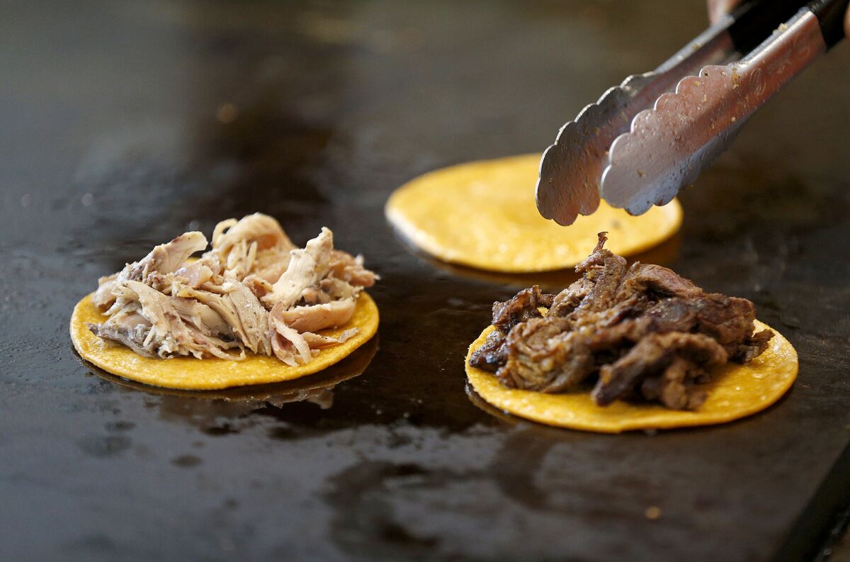 Rotisserie chicken and mesquite woodfire steak tacos on corn tortillas are prepared on a flat grill at Taco Mesita in Tustin.