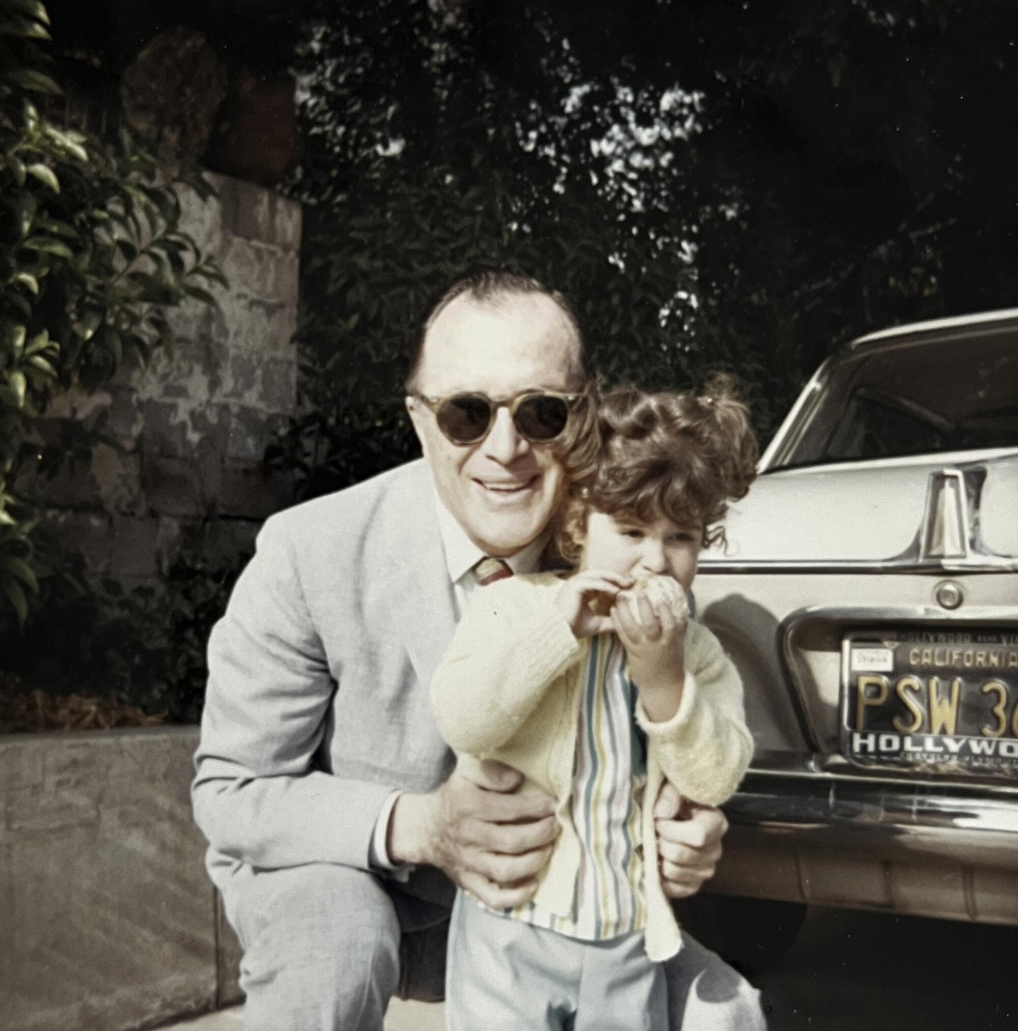 A man crouches down next to a car with a toddler