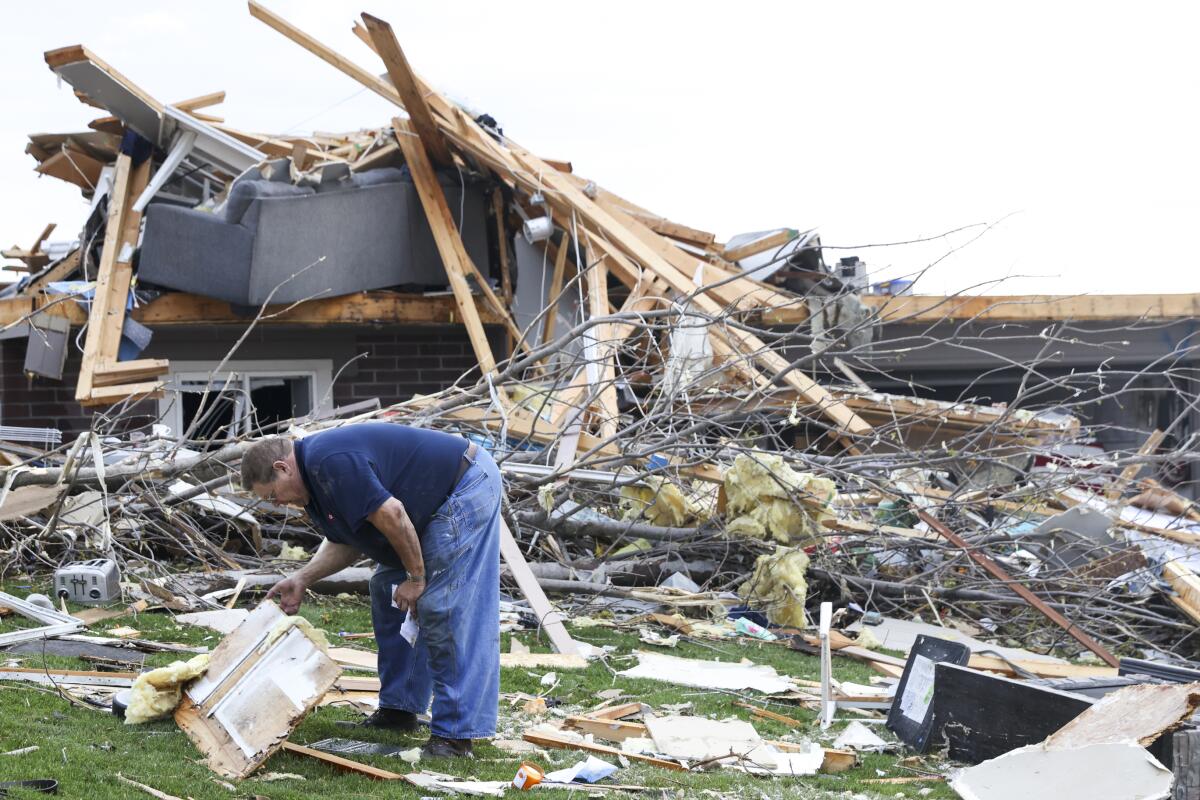 A man sifts through debris in front of a splintered, destroyed home. 