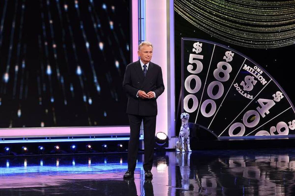 Pat Sajak in a dark suit standing on the stage of "Wheel of Fortune."