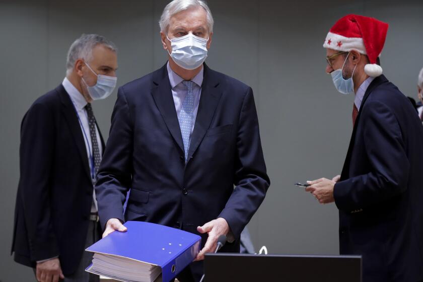 A colleague wears a Christmas hat as European Union chief negotiator Michel Barnier, center, carries a binder of the Brexit trade deal during a special meeting of Coreper, at the European Council building in Brussels, Friday, Dec. 25, 2020. European Union ambassadors convened on Christmas Day to start an assessment of the massive free-trade deal the EU struck with Britain. After the deal was announced on Thursday, EU nations already showed support for the outcome and it was expected that they would unanimously back the agreement, a prerequisite for its legal approval. (Olivier Hoslet, Pool via AP)