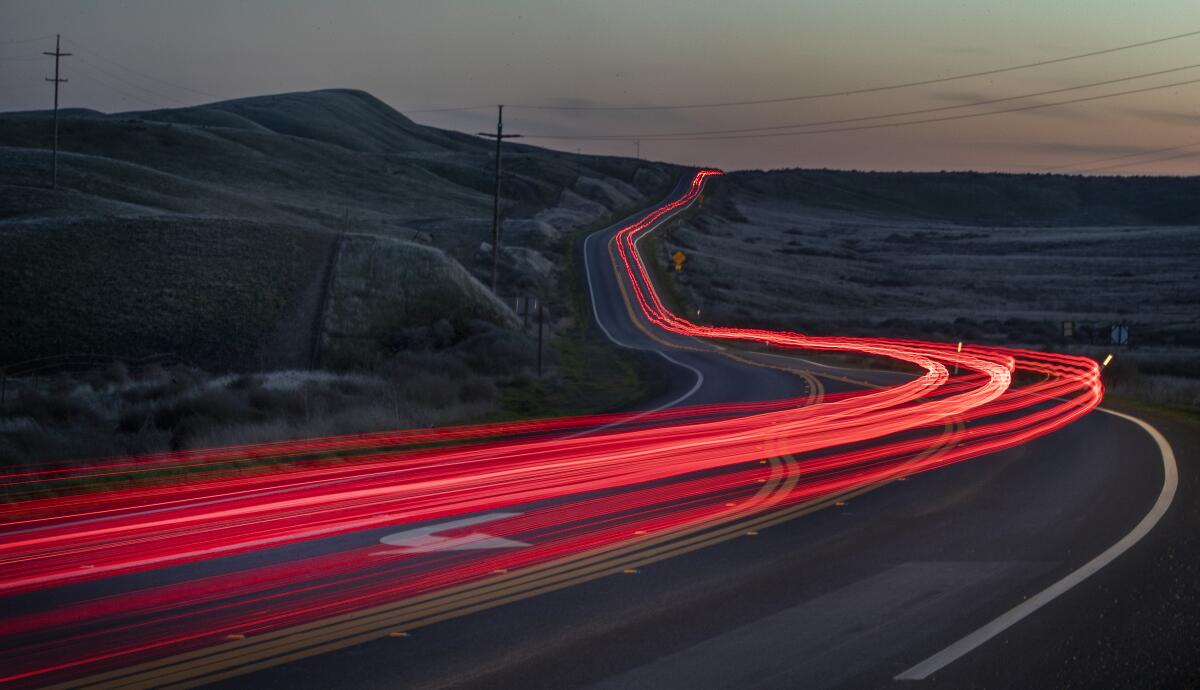 Taillights are seen as a red stream of light on a curving open road.