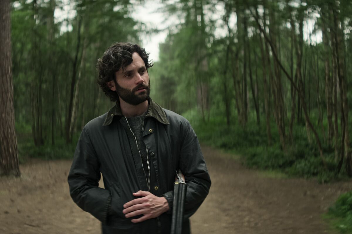 A man in a leather jacket walking with a shotgun in the forest.