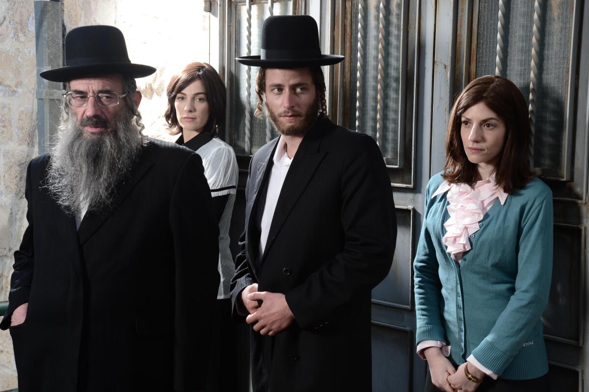 Four Orthodox Jews, two men and two women, standing in a doorway.