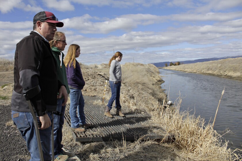 FILE - In this March 2, 2020, file photo, farmer Ben DuVal with his wife, Erika, and their daughters, Hannah, third from left, and Helena, fourth from left, stand near a canal for collecting run-off water near their property in Tulelake, Calif. The Klamath Basin, a vast and complex water system that spans Oregon and California, is in the throes of the worst drought in recorded history, with water flows in the tributaries of the Klamath River that are as low as they have been in a century. Federal officials are expected to announce the water allocations for the season this week and it's possible that farmers might not get any water at all. (AP Photo/Gillian Flaccus, File)