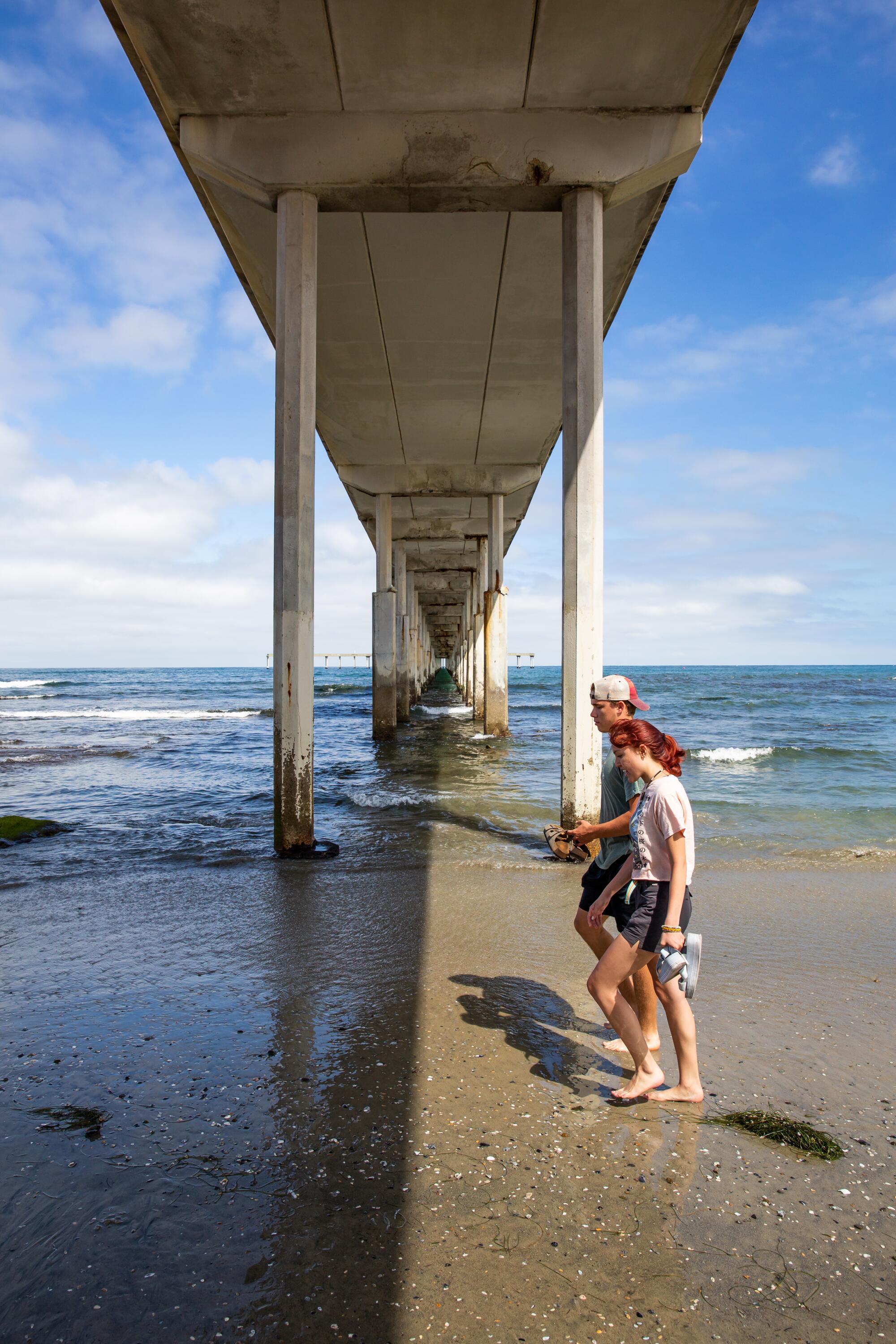 Evan Smith and Sanjannah Domnick walk beneath the Ocean Beach Pier on July 5, 2022.