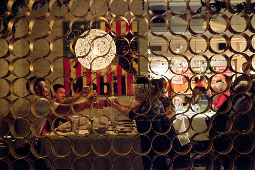 A view through an ornate window of diners raising their glasses in a toast.