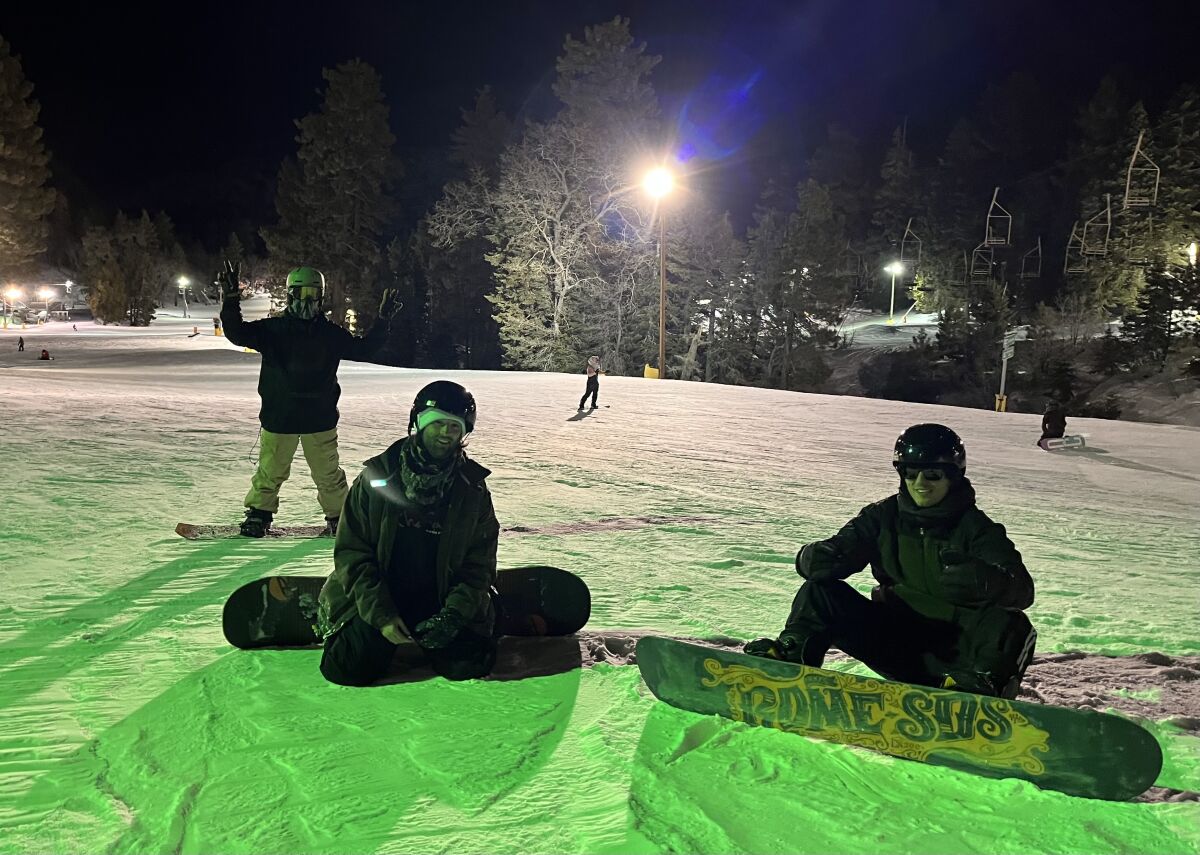 Three men on snowboards on a snowy hillside at night.