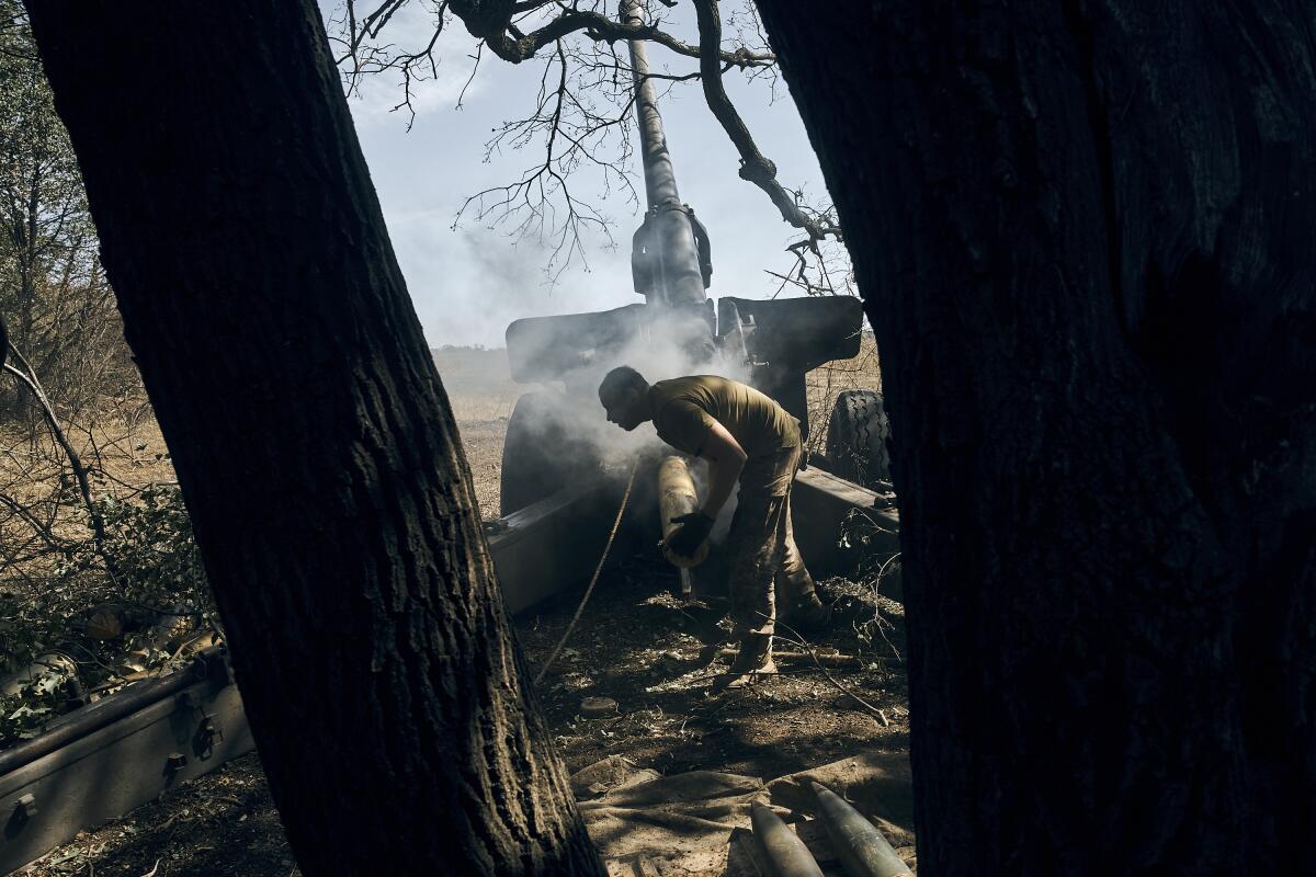 A soldier loads an artillery shell next to a tree