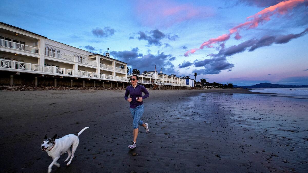 A woman and her dog make their way along the beach past the Rosewood Miramar Beach resort in Montecito.