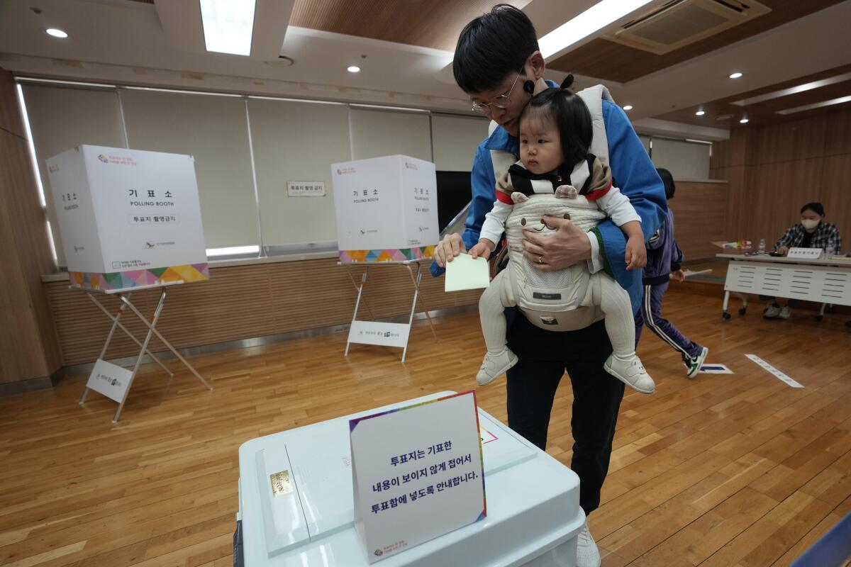 A man holds his daughter in a chest sling as he approaches a ballot box